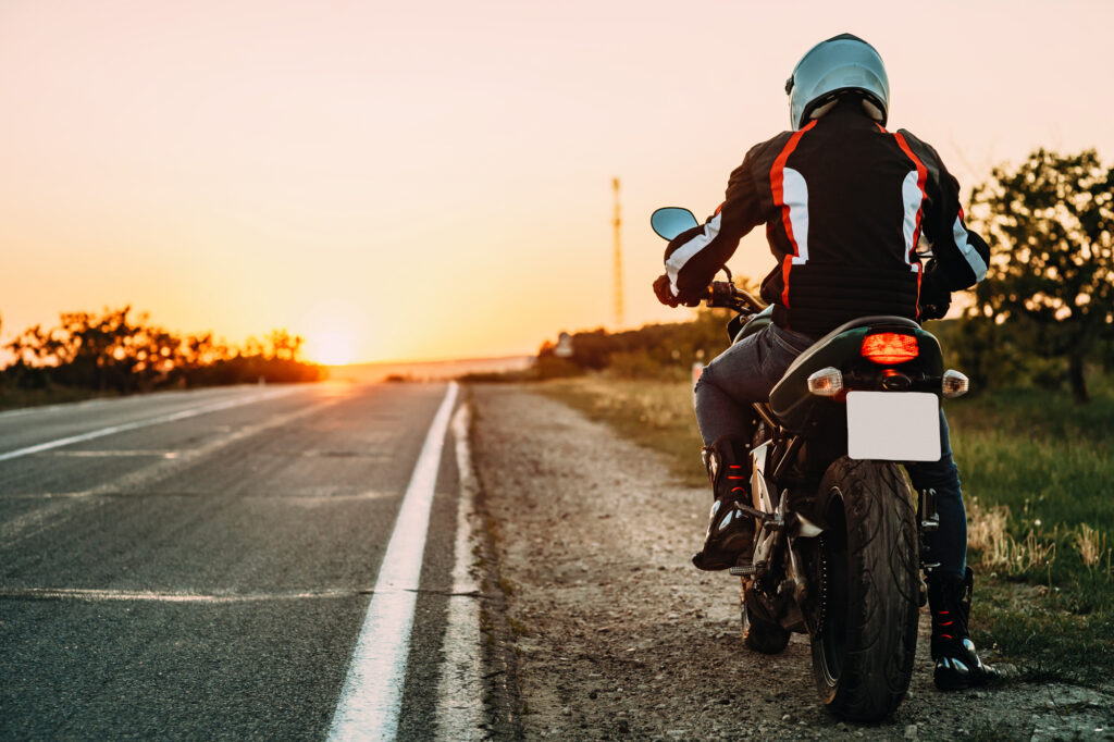 Motorradfahrer hält im Sonnenuntergang auf dem Seitenstreifen einer Landstrasse