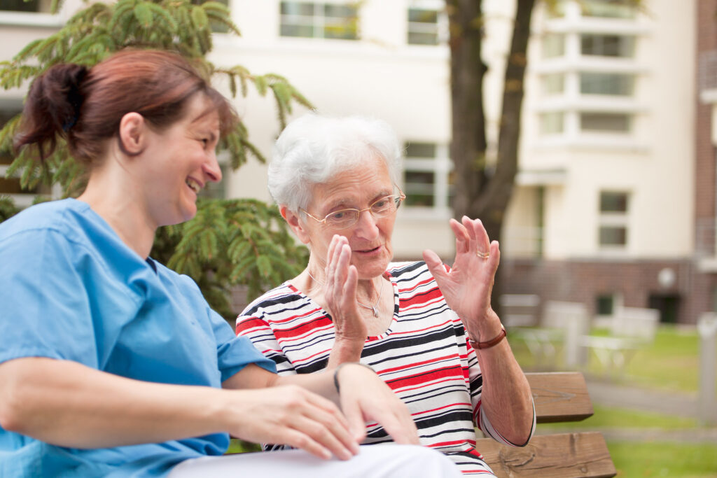 Pflegeschwester im Gespräch mit Seniorin im Park