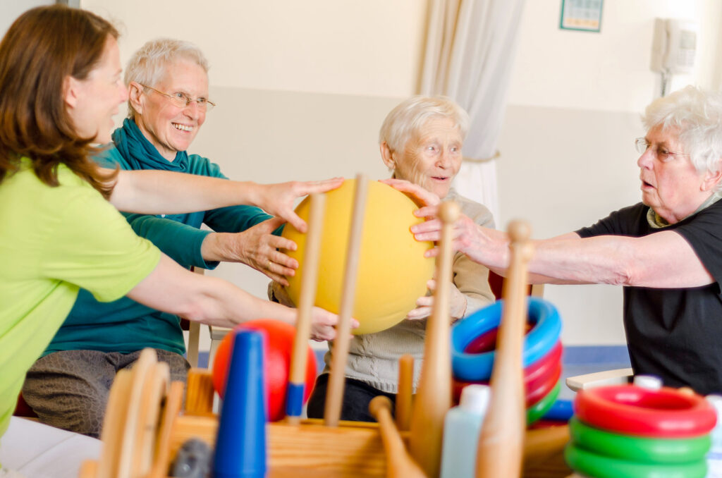 Gruppe von älteren dementen Menschen spielt zusammen mit dem Therapeuten Ball