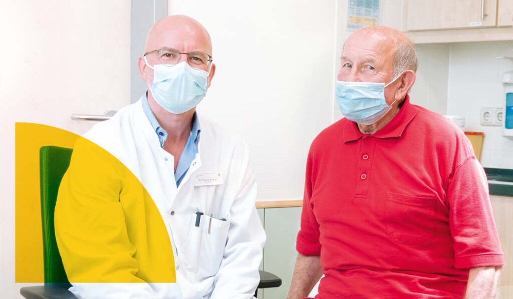 Dr. Thomas Bürkigt sitzt zusammen mit dem Patienten Herbert Pfau im Untersuchungszimmer